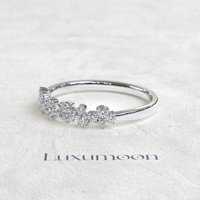 May include: A silver-toned ring featuring a cluster of small, round, clear stones set along the top half of the band. The band is smooth and polished. The word Luxumoon is printed in dark letters below the ring on the textured surface.