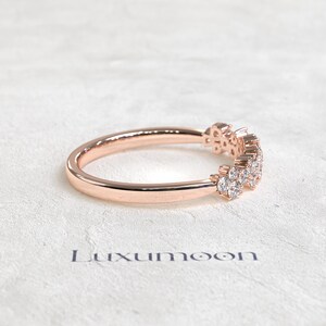 May include: A rose gold ring featuring a curved band set with a cluster of small, clear, round-cut stones along the top section. The metal has a polished, reflective finish. The word Luxumoon is printed in dark lettering below the ring.