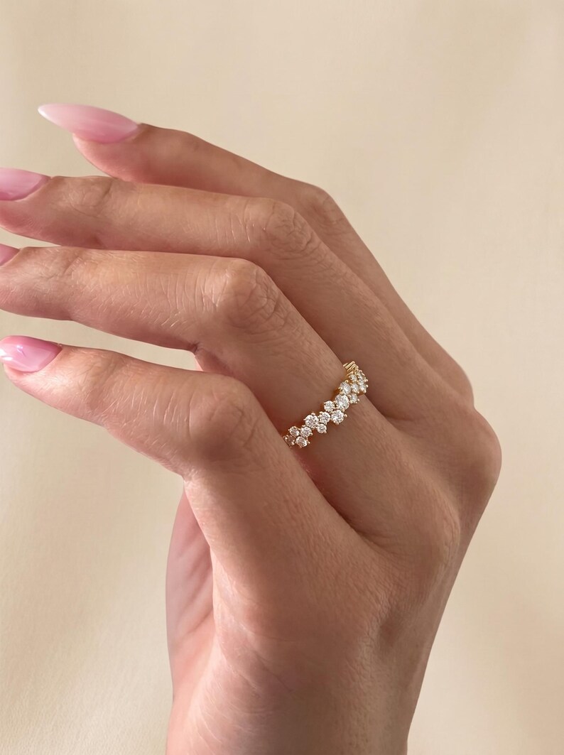 May include: A gold ring featuring a cluster of small, round, clear stones arranged in a continuous, slightly irregular band. The stones are set in a metallic gold frame that follows the contour of the stones, creating a textured, sparkling appearance.