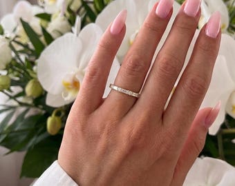 May include: A thin gold band ring featuring a repeating pattern of alternating baguette-cut and round-cut clear stones set along the entire circumference of the metal band, creating a continuous sparkling design around the finger.