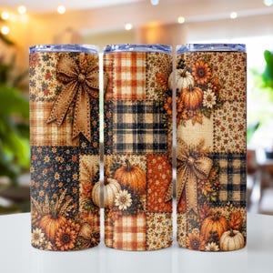 May include: A cylindrical tumbler featuring a patchwork design of autumn-themed patterns including orange and white pumpkins, sunflowers, wheat stalks, brown bows, and plaid squares in shades of orange, black, and tan on a textured background.