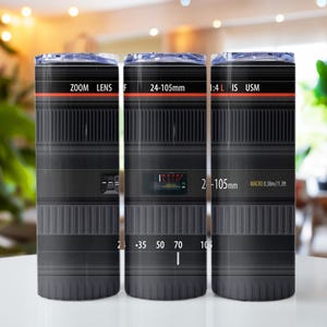 May include: Three stainless steel tumblers with a black and silver camera lens design. The text on the lens reads "ZOOM LENS F 24-105mm 1:4 L IS USM 2-105mm MACRO 0.38m/1.3f".