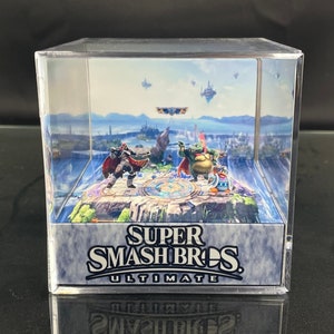 May include: A clear acrylic cube display case with a 3D image of a video game scene. The scene features two characters from the game Super Smash Bros. Ultimate, standing on a platform with a blue sky and clouds in the background. The text "SUPER SMASH BROS. ULTIMATE" is printed on the base of the cube.