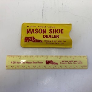 May include: A yellow rectangular vinyl sleeve with red text reading A GIFT FROM YOUR MASON SHOE DEALER and MASON SHOE MFG. CO. Chippewa Falls, Wis. A yellow plastic ruler is positioned below, measuring 6 inches in length with matching red text.