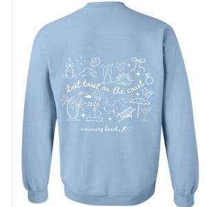 Puede incluir: Sudadera azul claro con un diseño blanco en la espalda. El diseño incluye el texto "Last toast on the coast 2025 rosemary beach, fl" y varias ilustraciones con temática de playa.