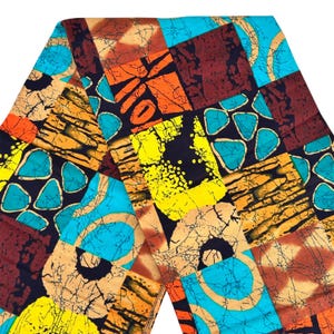 May include: A colorful fabric with a patchwork design. The pattern features squares and shapes in shades of orange, yellow, blue, and brown against a black background. The fabric has a textured appearance.