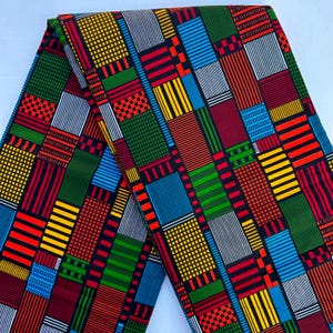 May include: A vibrant fabric with a geometric pattern. The design features a patchwork of colorful rectangles and squares in red, yellow, green, blue, and white, set against a dark background. The fabric is folded, showcasing the repeating pattern.