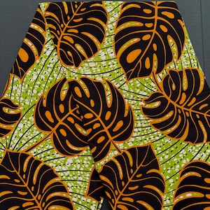May include: Black and orange fabric with a repeating pattern of large tropical leaves on a green and white background.