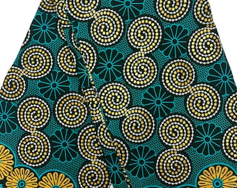 May include: A folded fabric with a repeating pattern of gold and white spiral designs on a teal and black background. The fabric also features a border of gold floral designs. The fabric is likely used for clothing or home decor.