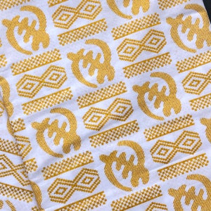 May include: White fabric with a repeating pattern of gold Adinkra symbols. The symbols include the Gye Nyame symbol, a symbol of the omnipotence of God, and other geometric shapes. The fabric is likely used for clothing or decorative purposes.