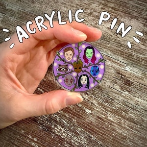 May include: A round acrylic pin featuring characters from Guardians of the Galaxy. The pin has a purple background with character portraits and the text "ACRYLIC PIN" in a white bubble font.
