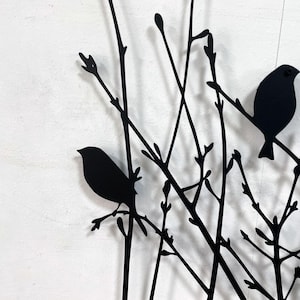 以下が含まれることがあります： 黒い金属製の壁の芸術で、枝にとまっている鳥のシルエットが特徴です。このアートワークは、家の装飾に適した、自然に焦点を当てたミニマリストデザインを示しています。鳥と枝は、白い背景に対して対照的な黒色です。