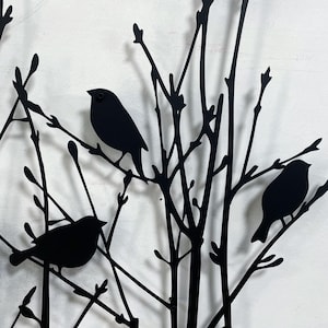 以下が含まれることがあります： 枝にとまる鳥のシルエットが特徴の黒い金属製の壁掛けアート。このアートワークは、複数の鳥がいる様式化された木を描いており、自然にインスパイアされた装飾品を作り出しています。鳥と枝はすべて黒一色です。
