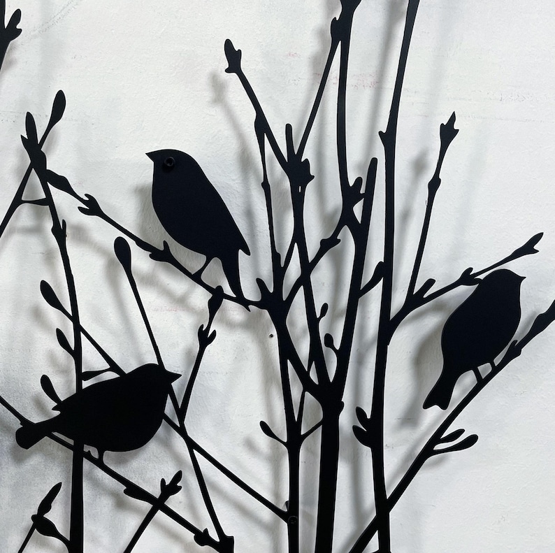 以下が含まれることがあります： 枝にとまる鳥のシルエットが特徴の黒い金属製の壁掛けアート。このアートワークは、複数の鳥がいる様式化された木を描いており、自然にインスパイアされた装飾品を作り出しています。鳥と枝はすべて黒一色です。