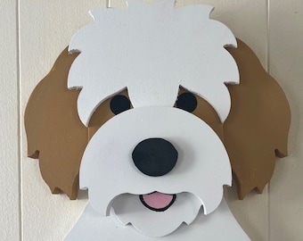 May include: A wooden dog-shaped wall hook with a white face and head, brown ears, and a black nose. The dog's mouth is pink, and it has two black hooks below. The names "Fozzie" and "Pooh" are written above the hooks.
