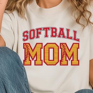 Könnte beinhalten: Ein weißes T-Shirt mit dem Text "SOFTBALL MOM" in roten und gelben Buchstaben mit einem Baseball-Stich-Design.