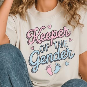 May include: A white t-shirt with the text "Keeper of the Gender" in pink and blue lettering. The text is surrounded by small pink hearts. There are two baby footprints, one pink and one blue, below the text.