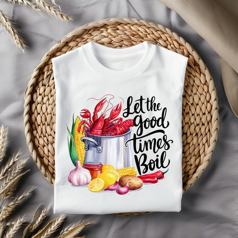 May include: White t-shirt with a graphic of a pot of crawfish, corn on the cob, garlic, lemons, and red peppers. The text "Let the good times boil" is written in black cursive lettering.