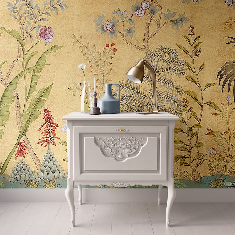 May include: White nightstand with a carved design on the front, featuring a single drawer. The nightstand is against a yellow wall with a floral wallpaper pattern. A lamp, vase, and other decorative items are on top of the nightstand.