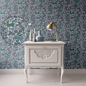 May include: A white painted wooden nightstand with a single drawer and ornate carvings. The nightstand has cabriole legs and sits in front of a wall covered in a floral wallpaper with a repeating pattern of green and pink stylized animals.