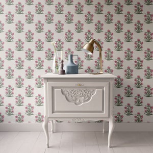 Puede incluir: Una mesita de noche blanca con un dise&ntilde;o tallado en el caj&oacute;n delantero. La mesita de noche tiene una l&aacute;mpara con base y pantalla doradas, un jarr&oacute;n de vidrio transparente con una sola flor blanca, una vela y un jarr&oacute;n de cer&aacute;mica azul en la parte superior.
