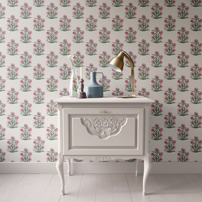 Puede incluir: Una mesita de noche blanca con un dise&ntilde;o tallado en el caj&oacute;n delantero. La mesita de noche tiene una l&aacute;mpara con base y pantalla doradas, un jarr&oacute;n de vidrio transparente con una sola flor blanca, una vela y un jarr&oacute;n de cer&aacute;mica azul en la parte superior.