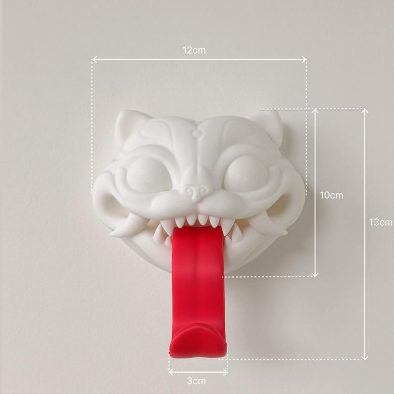 May include: A white cat-shaped wall hook with a red tongue, measuring 12cm wide, 10cm high, and 3cm deep. The hook is 5 inches tall. The cat has sharp teeth and is mounted on a white wall. The overall height is 13cm.