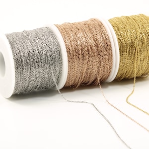 May include: Three spools of chain, one silver, one rose gold, and one gold. The chain is on white spools and the background is white.