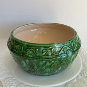 May include: A green ceramic planter with a floral design. The planter has a light brown interior and a glossy finish.