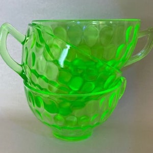 May include: Two green glass cups with a textured, bubble-like design. The cups are stacked on top of each other.