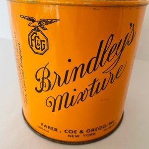 May include: Orange metal tin with black text that reads "Brindley's Mixture" and "Faber, Coe & Gregg, Inc. Chicago, New York". The tin also features a black eagle logo with the letters "FCG" inside a circle.