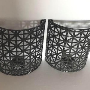 May include: Two black, semi-circular wall planters. Each planter has a geometric, openwork design. The planters are made of a dark material and are designed to be mounted on a wall. The interior of the planters is not visible.