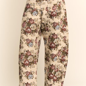 May include: Beige floral print pants with a high waist and wide legs. The pants feature a repeating pattern of roses in shades of red, pink, blue, and green. The pants are paired with brown heeled boots.