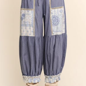 May include: Blue and white checkered pants with a drawstring waist and decorative patches. The patches feature a floral design. The pants have a gathered, ruffled hem at the ankles. The pants are approximately 38 inches long.