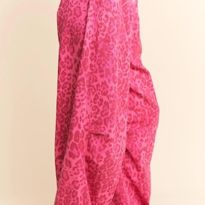 Puede incluir: Pantalones anchos de color rosa brillante con estampado de leopardo. Los pantalones tienen cintura con cordón y bolsillos. El modelo lleva zapatillas deportivas con detalles en marrón y rosa.
