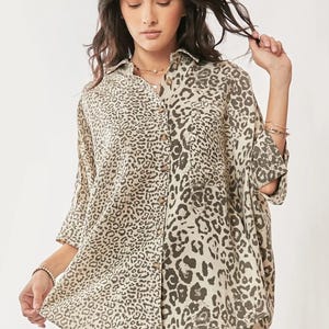 Puede incluir: Camisa abotonada con estampado de leopardo en tonos beige y marrón. La camisa tiene cuello, mangas tres cuartos y corte holgado. La modelo lleva la camisa con pantalones verde oliva.