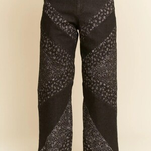 Peut inclure: Jean en denim noir avec des panneaux à motifs floraux. Le jean a une coupe droite et un ourlet brut. Le motif floral est de couleur gris clair. Le modèle porte des baskets rouges avec des lacets et des rayures blanches.