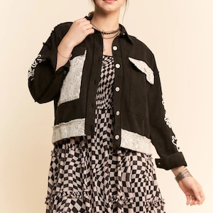 May include: Black corduroy jacket with white lace trim and embroidered detailing. The jacket is worn over a black and white checkered dress. The dress has a tiered, ruffled skirt. The outfit is accessorized with jewelry.
