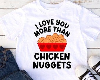 May include: White t-shirt with a black graphic that says "I love you more than chicken nuggets". The graphic features a red bowl with chicken nuggets and hearts.