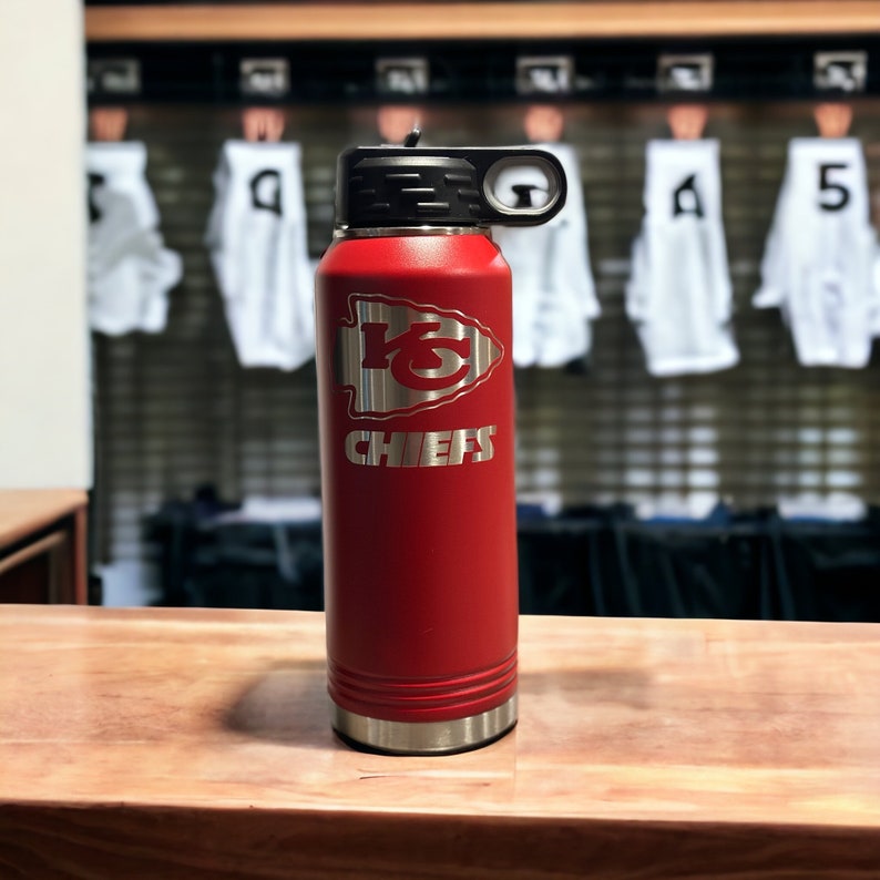 May include: Red stainless steel water bottle with a black lid and handle. The bottle has a silver band around the bottom and a silver Chiefs logo with the word "Chiefs" underneath.