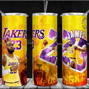 May include: Three yellow and purple stainless steel tumblers with a basketball theme. The tumblers feature a graphic of basketball player LeBron James wearing a Los Angeles Lakers jersey with the number 23. The text "LAKERS" and "JAMES" are featured on the tumblers.
