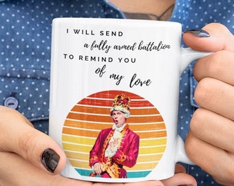 May include: White ceramic mug featuring a quote: "I will send a fully armed battalion to remind you of my love." The mug has a retro design with a portrait of a man in a red coat and crown against a sunset background. The mug is held by a person.