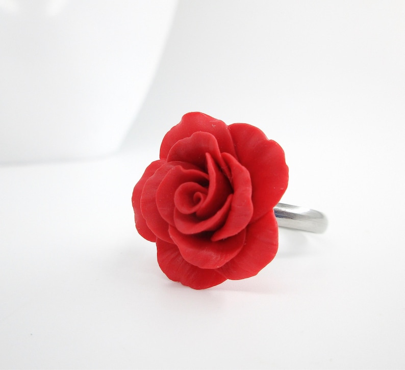 May include: A red rose ring with a silver band. The rose is made of polymer clay and has a realistic appearance.
