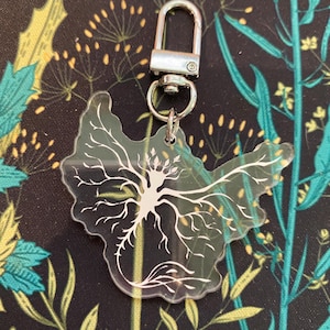 May include: A clear acrylic keychain with a white outline of a tree root system. The keychain has a silver metal clasp.