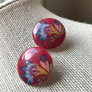 May include: A pair of red button earrings with a floral pattern in blue, yellow, and pink.