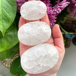 May include: Three white, smooth, oval-shaped selenite stones of varying sizes. The stones have a cloudy, translucent appearance.