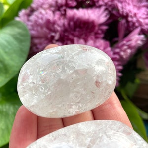 May include: Two white, clear quartz crystal palm stones with a sparkly, iridescent finish. The stones are smooth and polished.