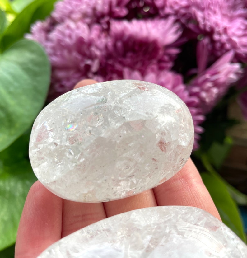 May include: Two white, clear quartz crystal palm stones with a sparkly, iridescent finish. The stones are smooth and polished.