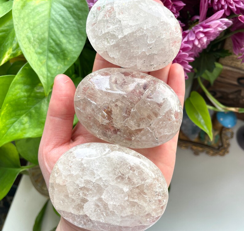 May include: Three clear quartz crystal palm stones. The stones are smooth and have a cloudy, milky appearance.