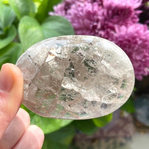 May include: A clear, oval-shaped crystal with a unique, fractured, and iridescent appearance. The crystal has a smooth, polished surface and is a natural gemstone.
